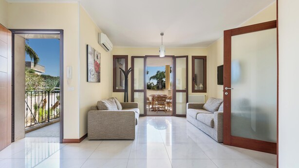 A spacious living area with two sofas, a dining table, and a view through a glass door to an outdoor balcony.