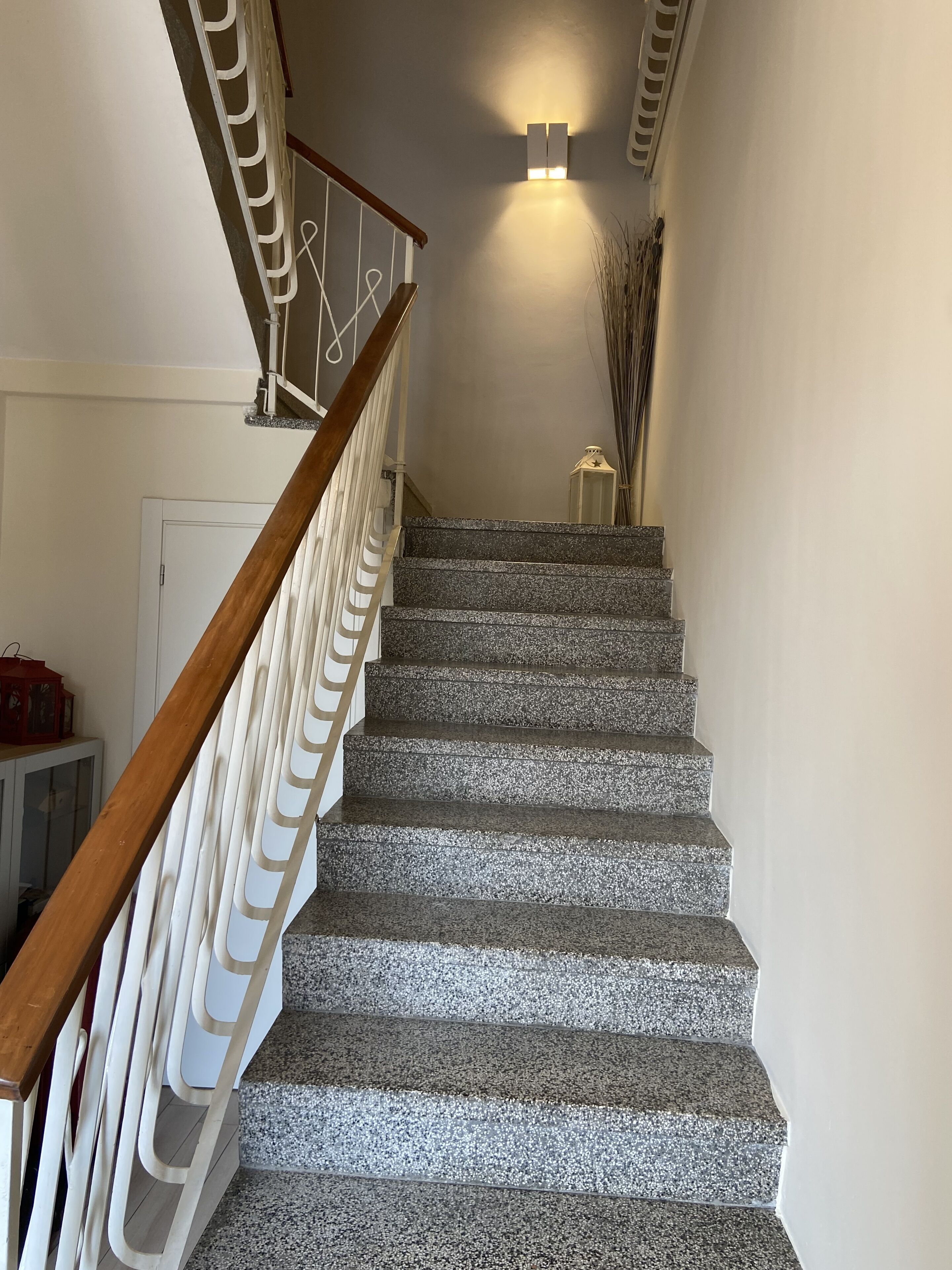 Un escalier avec une rampe en bois et des balustrades blanches, menant à un palier où est fixée une applique murale.