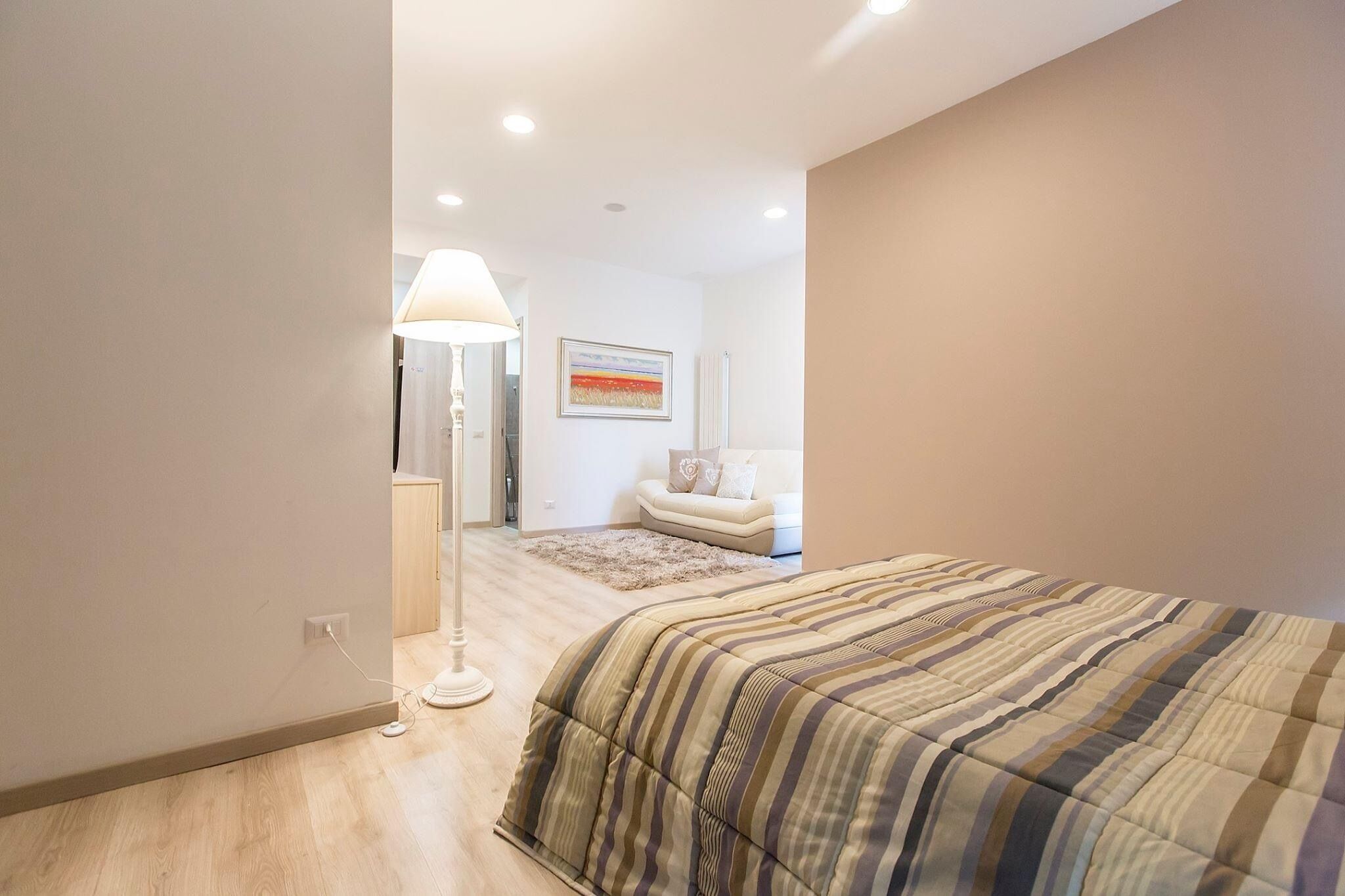 Un dormitorio moderno con una cama grande, una lámpara de noche y un pequeño sofá al fondo.