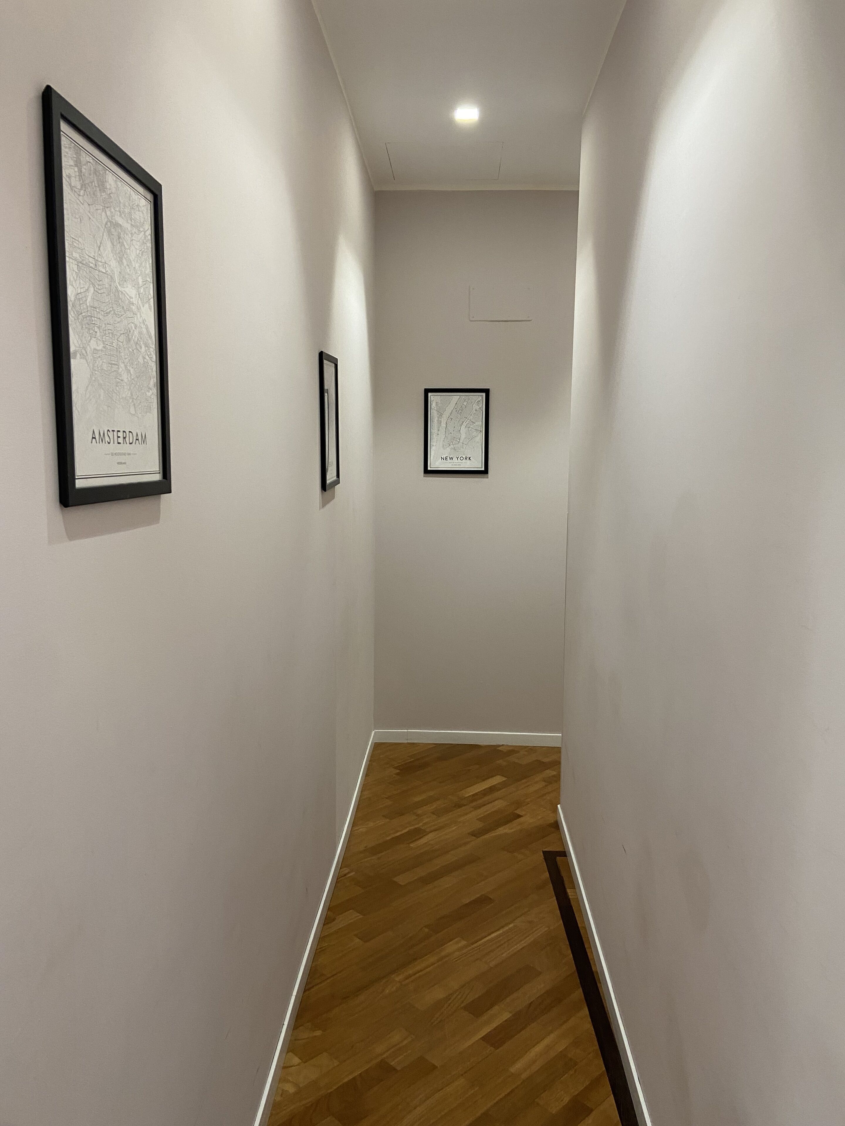 A hallway with two framed maps labeled 'Amsterdam' and 'New York'.