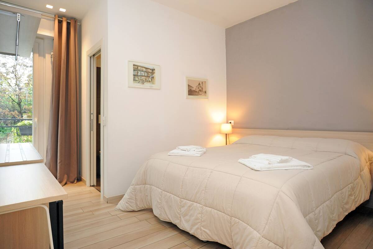 A hotel room with a bed, a desk, and a window with curtains.