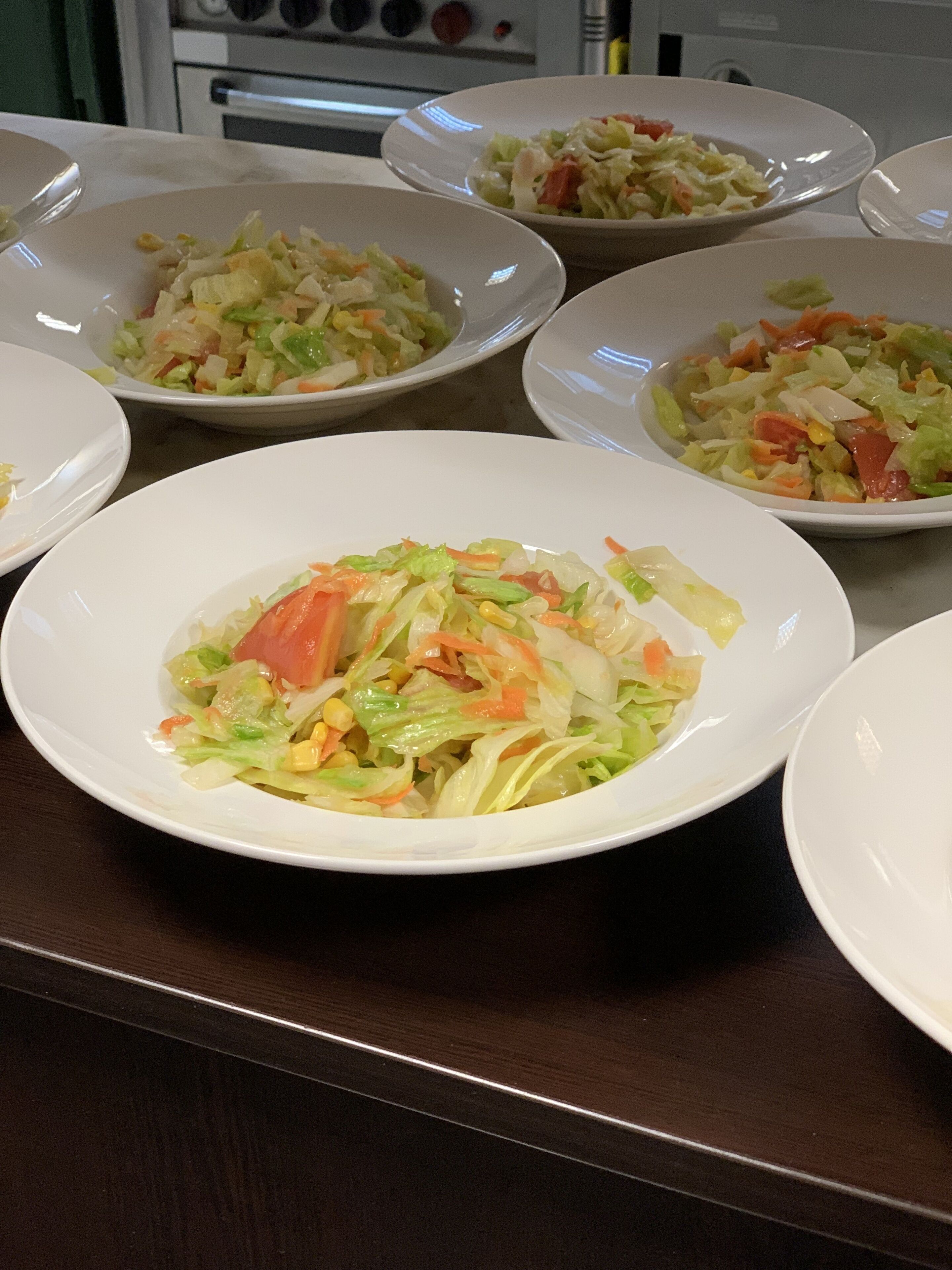 A table with multiple white plates containing a salad with various vegetables.