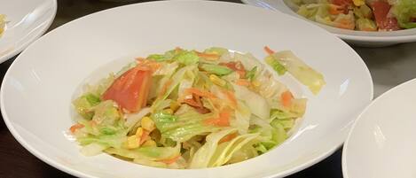 A table with multiple white plates containing a salad with various vegetables.