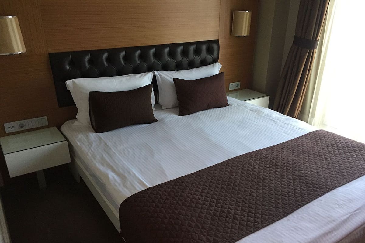 A neatly made bed with a tufted headboard, two bedside tables with lamps, and a window with curtains.