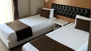 A hotel room with two beds, a nightstand, a painting of a sunset, and a window with curtains. - City Hotel Plovdiv (Plovdiv)