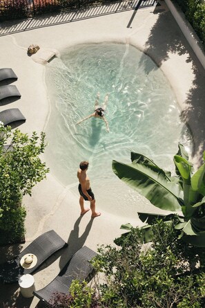 Una piscina con agua cristalina, rodeada de sillones de descanso y plantas tropicales.