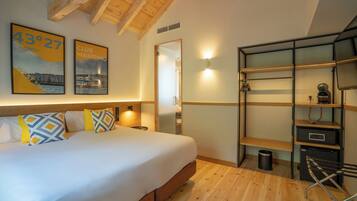 Habitación de hotel con una cama grande, vigas de madera en el techo, un espejo, una repisa con un hervidor y dos cuadros en la pared.