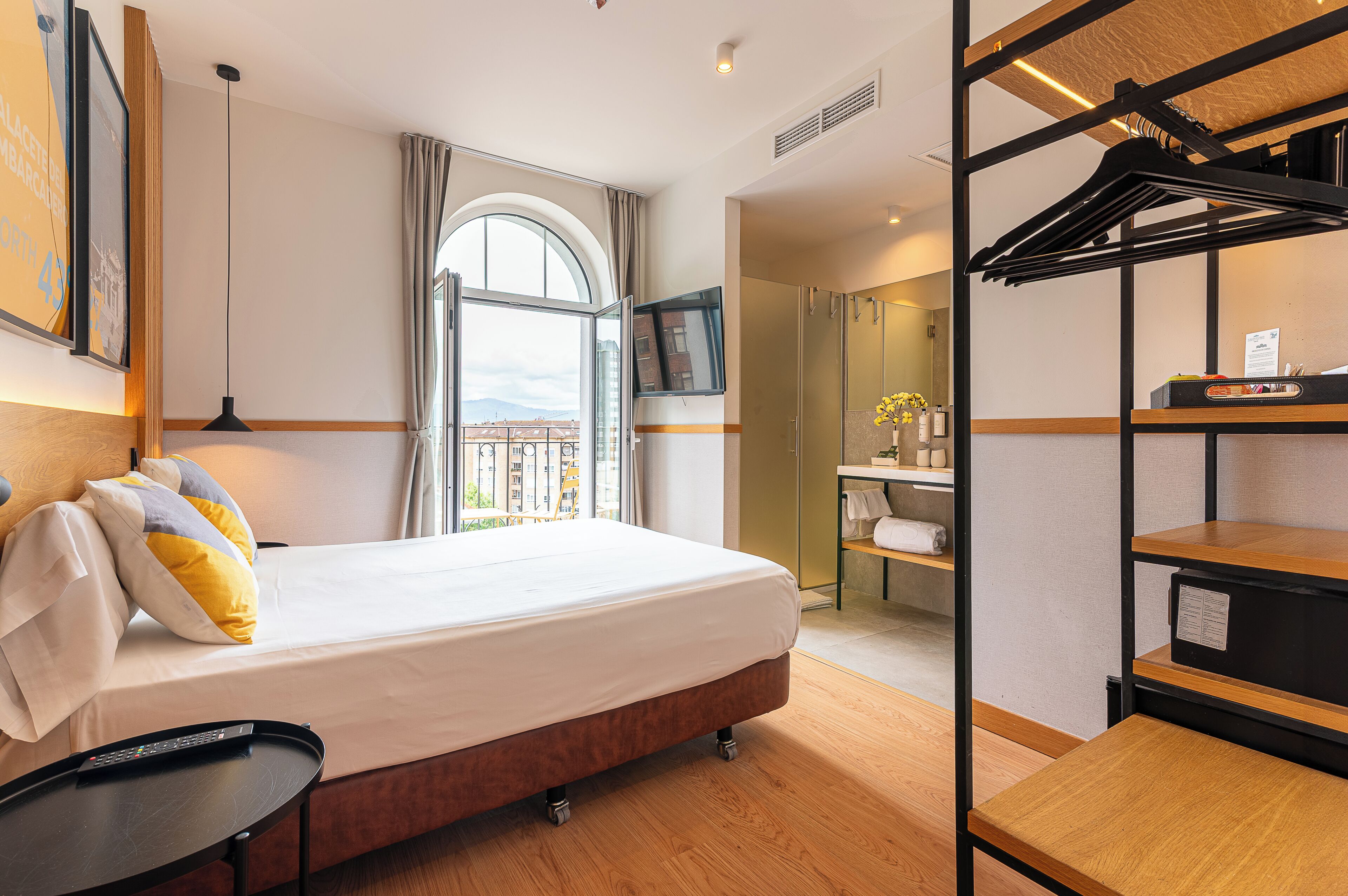 A hotel room with a bed, a desk, a TV, a window with a view, and a coat rack.
