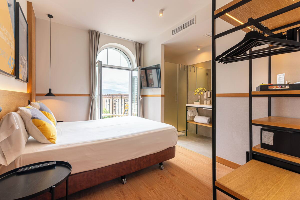 Una habitación de hotel con cama, escritorio, televisor, ventana con vistas y perchero.