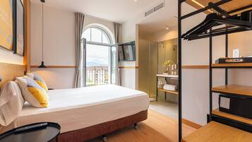 A hotel room with a bed, a desk, a TV, a window with a view, and a coat rack.