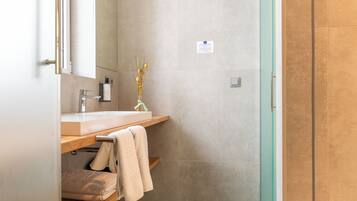 A modern bathroom with a wooden vanity, a mirror, a vase with branches, and a towel rack.