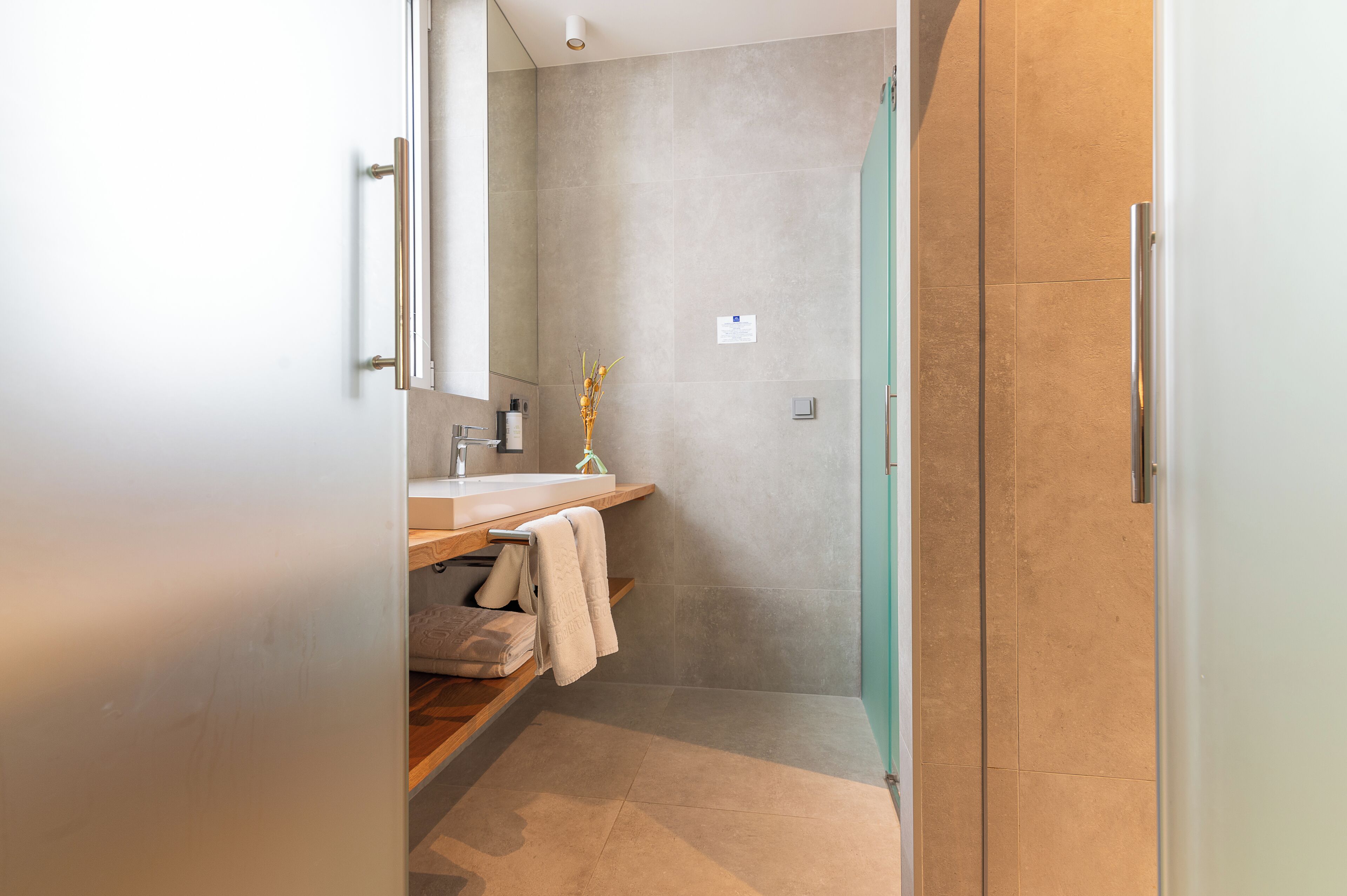 Un baño moderno con tocador de madera, espejo y zona de ducha.