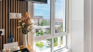 Una habitación con un ventanal amplio, un televisor de pantalla plana, un jarrón con flores secas y vistas a edificios y zonas verdes.