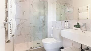 Un baño moderno con ducha de vidrio, inodoro blanco, lavamanos con espejo y perchero para toallas.