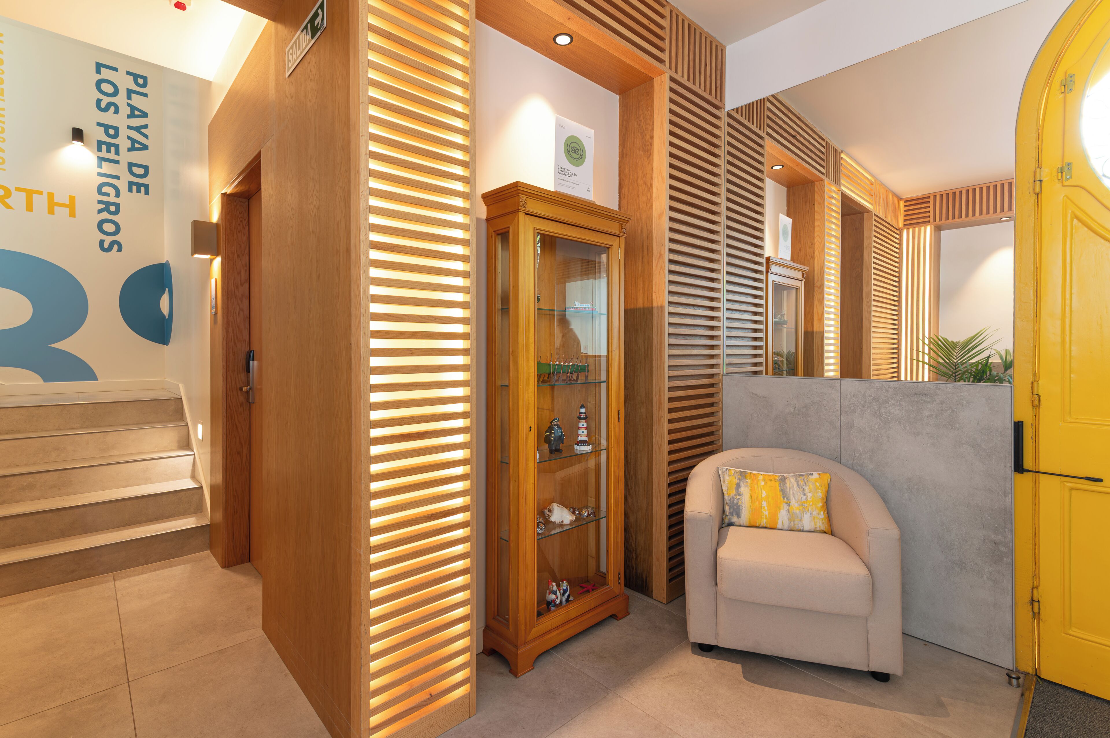 A hotel lobby with a wooden staircase, a glass display cabinet, a beige sofa, and a yellow door.