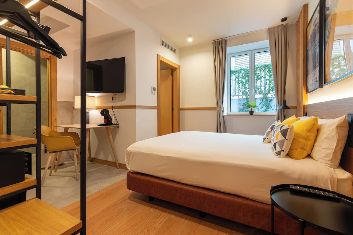Ein Hotelzimmer mit Bett, Schreibtisch, Stuhl, Fernseher und einem Fenster mit Vorhängen.