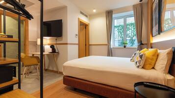 Habitació d'hotel amb un llit, escriptori, cadira, televisió i finestra amb cortines.