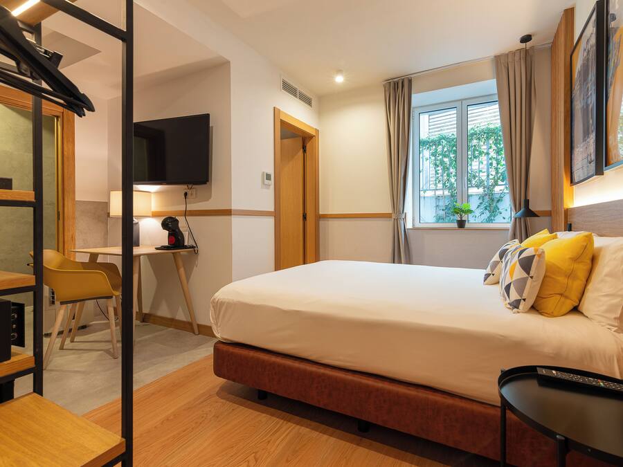 Habitació d'hotel amb un llit, escriptori, cadira, televisió i finestra amb cortines.