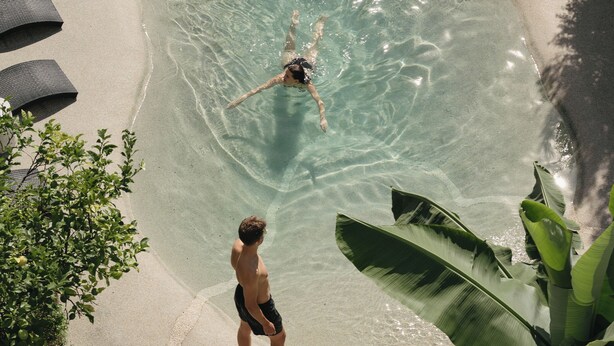 Una piscina cristalina con sillas de descanso y una persona nadando.