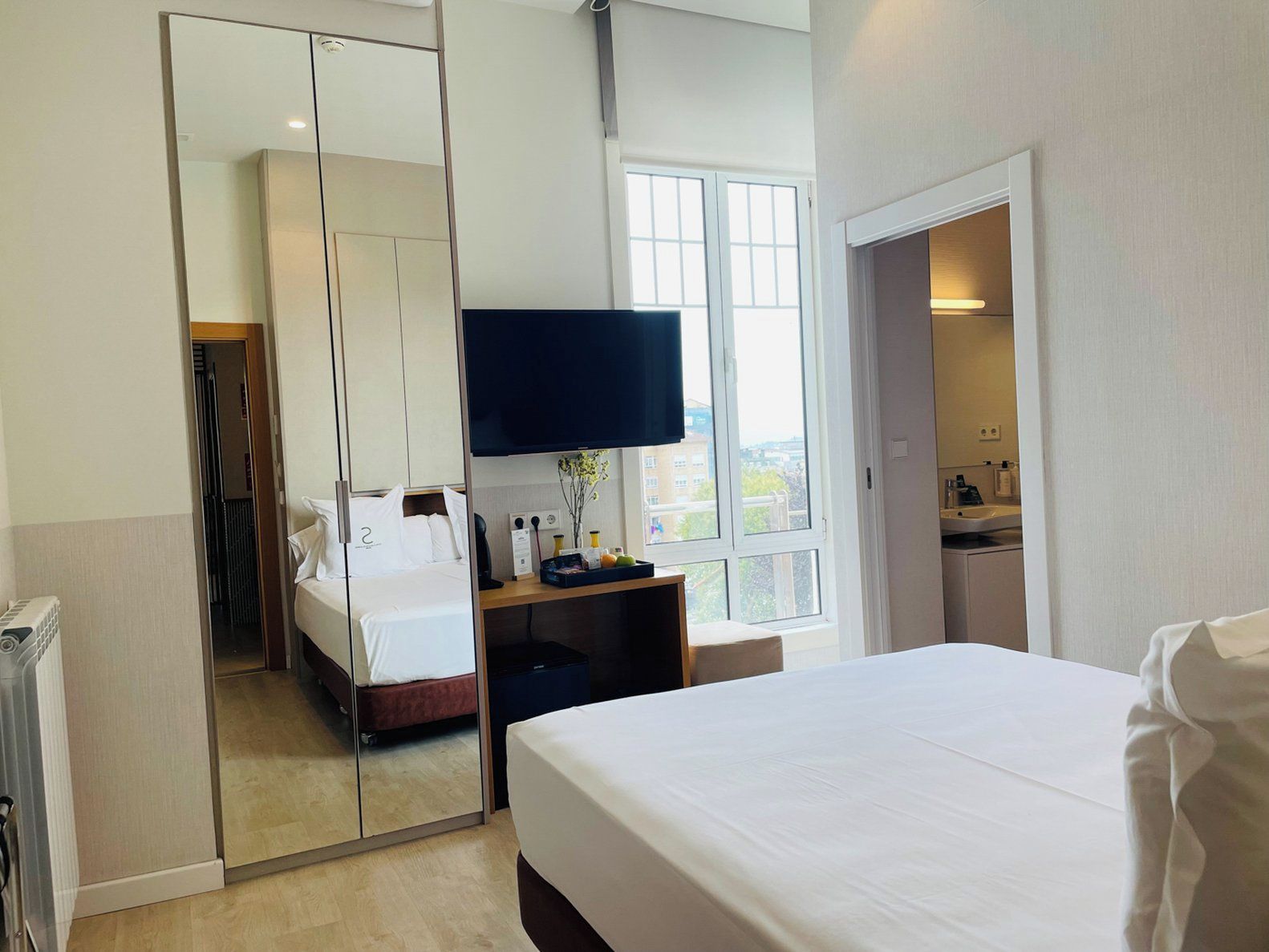 Ein Hotelzimmer mit Bett, Fernseher, Schreibtisch mit Vase und Fenster mit Blick.