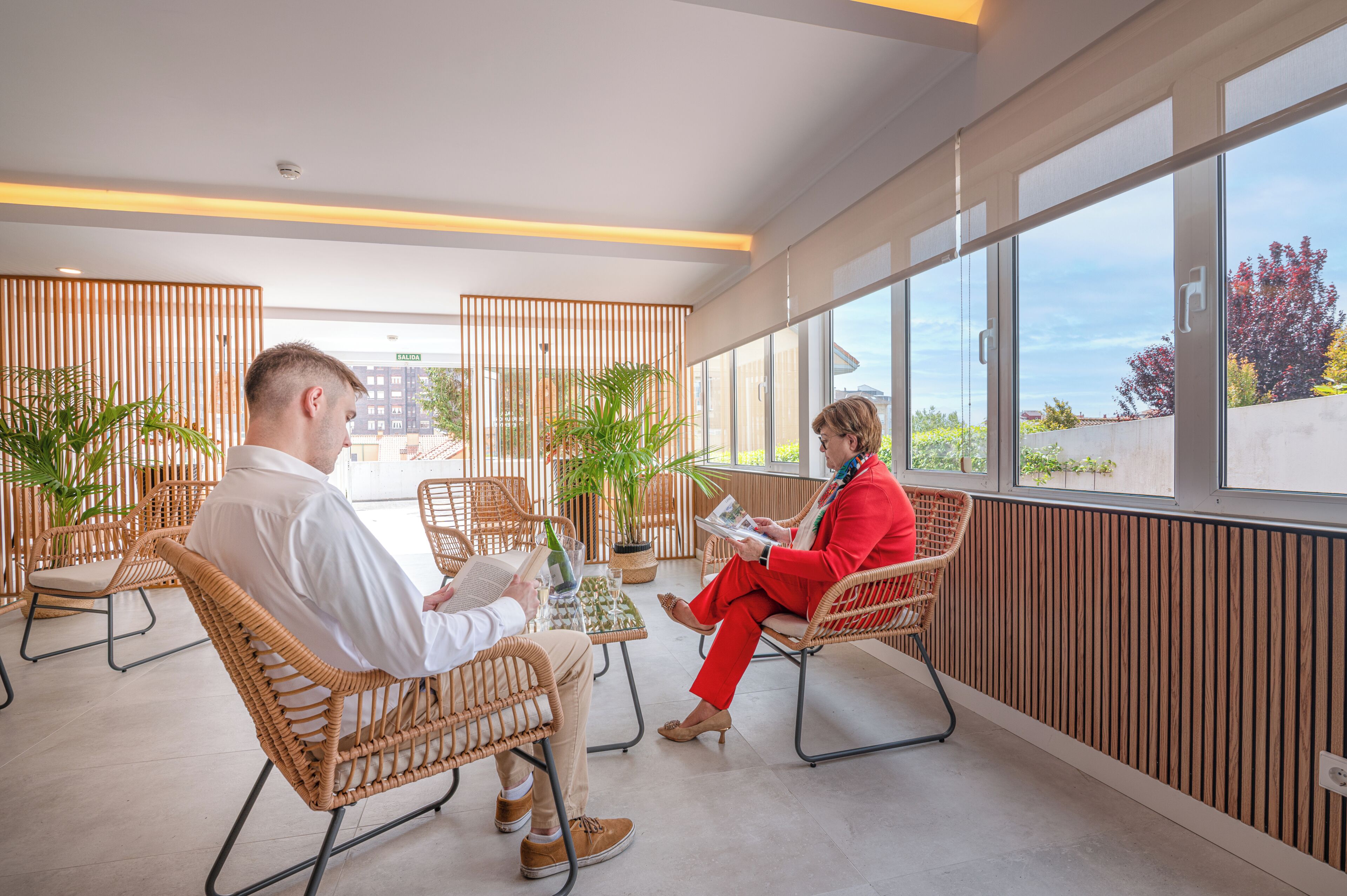 A modern indoor space with wicker chairs, potted plants, and large windows offering a view of the outside.