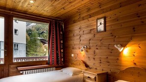 A wooden cabin room with two beds, a window with curtains, a radiator, and a wall-mounted light fixture. - Central apartment, near slopes, 10 pers, WiFi (Val-d'Isère)