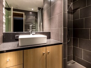Ein modernes Badezimmer mit einem weißen Waschbecken, Holzschränken und dunkel gefliesten Wänden.