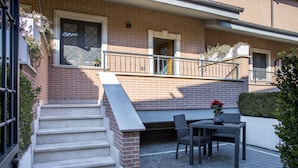 Un bâtiment en briques avec un escalier menant à un balcon. On trouve une table et des chaises sur le balcon.