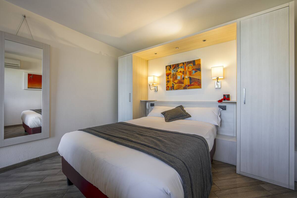 A hotel room with a large bed, a mirror, a painting on the wall, and a wardrobe.