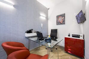 A modern office with a glass desk, red chairs, a printer, and a mounted TV. - Borgo Aureo (Rome)
