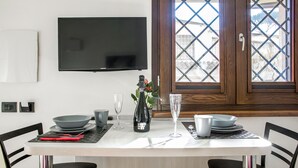 Un coin repas avec une table dressée pour deux personnes, un téléviseur fixé au mur et une fenêtre donnant sur l’extérieur.