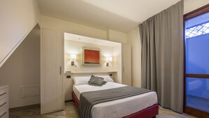 Une chambre d’hôtel moderne, équipée d’un lit, d’une table de chevet, d’une lampe fixée au mur et d’une fenêtre avec des rideaux.