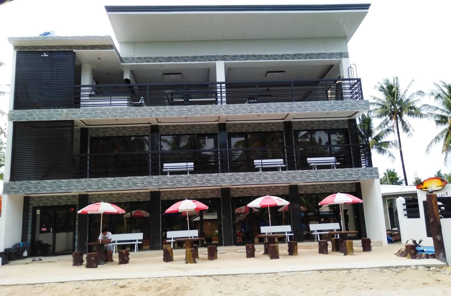 A multi-story building with a modern design, featuring a balcony on the upper floor and outdoor seating with umbrellas.