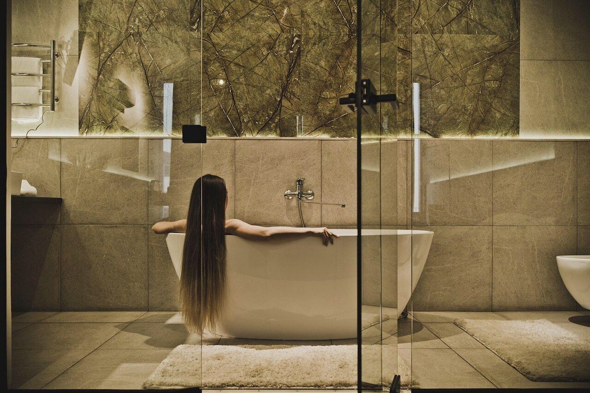 Eine Frau in einer Badewanne mit Glasabtrennung, Handtuchhalter und Marmorwand.