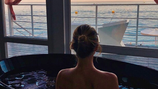 A person in a bathtub with a view of the sea through large windows. - Beach Club Odessa Hotel (Odesa)