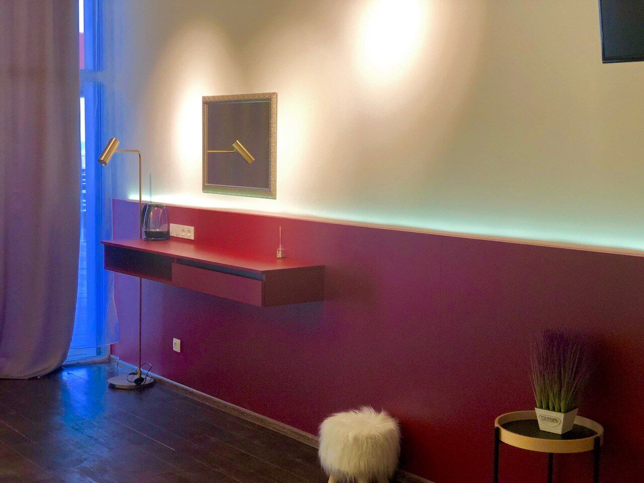 Ein modernes Zimmer mit einer roten Akzentwand, einer kleinen Ablage mit einem Radio, einer Topfpflanze und einem flauschigen weißen Gegenstand auf dem Boden.