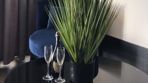 A potted plant with long green leaves on a round table, two empty wine glasses, and a blue chair in a room with dark curtains. - Beach Club Odessa Hotel (Odesa)