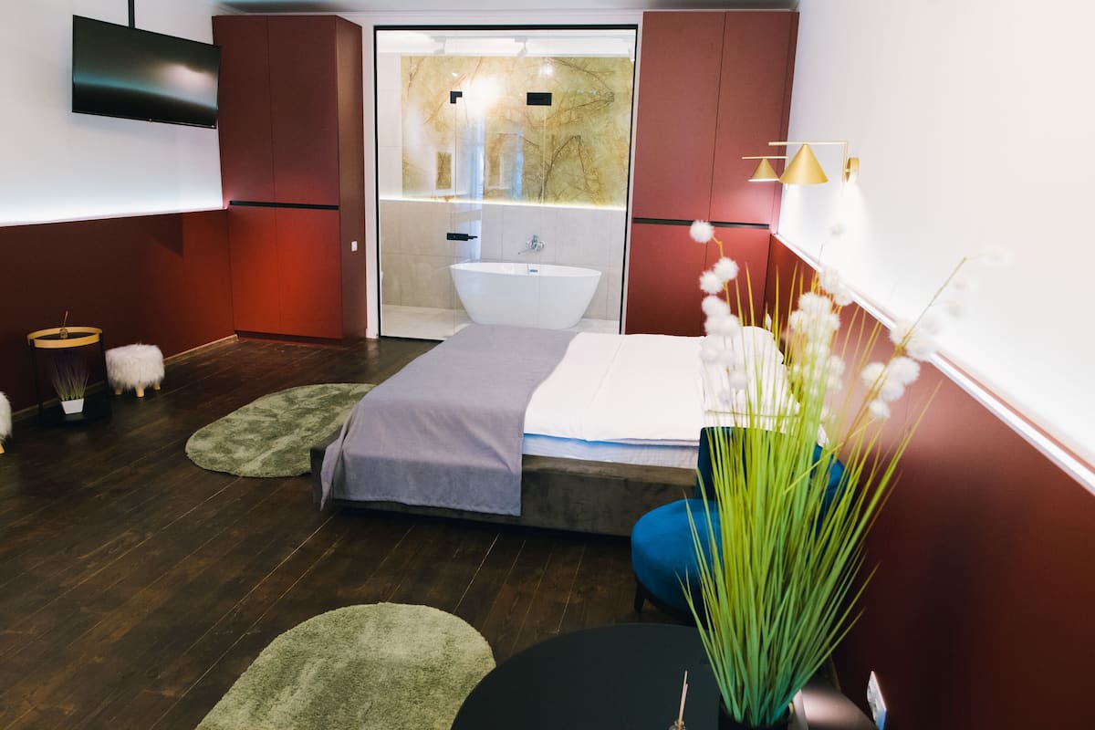Ein modernes Schlafzimmer mit einem Bett, einem großen Spiegel, einem Fernseher und einem Badezimmer mit einer Badewanne.