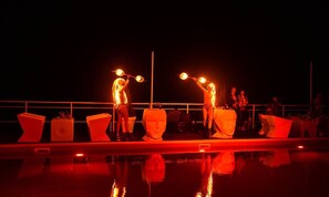 A nighttime outdoor event with performers on a stage, illuminated by red lighting, and a reflective pool in the foreground. - Beach Club Odessa Hotel (Odesa)
