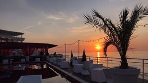 A sunset view from a deck with white chairs and a palm tree, overlooking the sea. - Beach Club Odessa Hotel (Odesa)