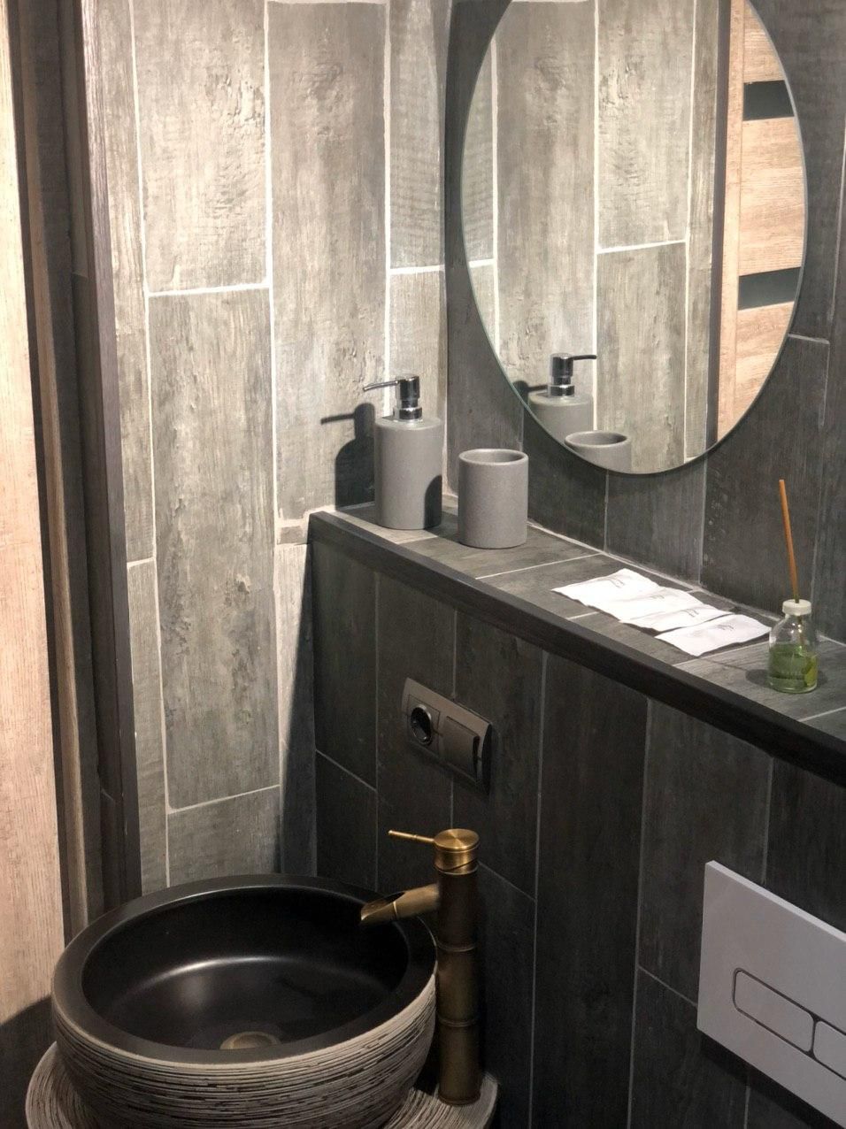 Ein modernes Badezimmer mit einem runden Spiegel, einem schwarzen Waschbecken und einem Handtuchspender.