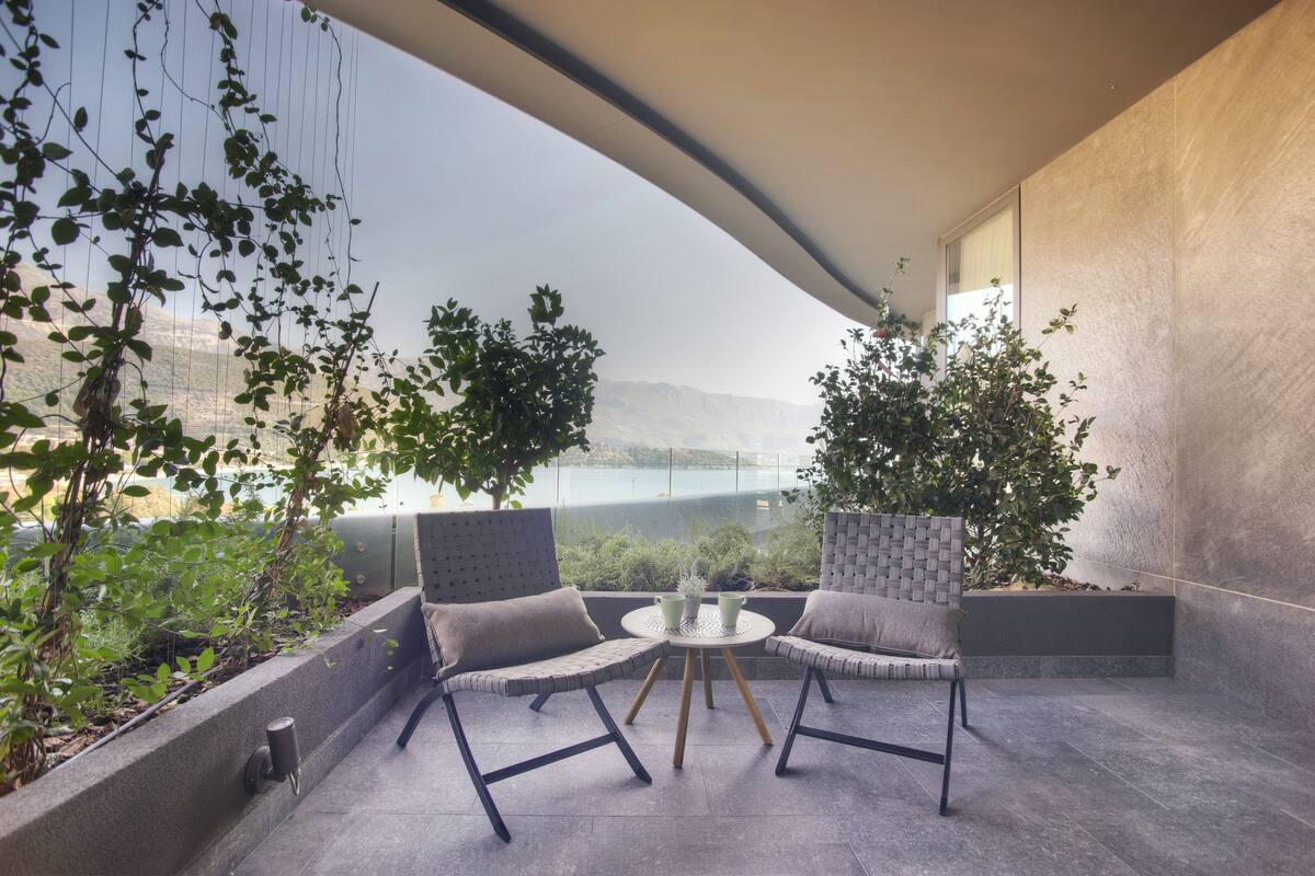 A modern outdoor seating area with two cushioned chairs and a small table, surrounded by plants and overlooking a scenic view.
