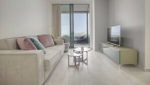 A modern living room with a sofa, a coffee table, a TV on a stand, and a view through a glass door. - Royal Gardens Paradise (Budva)