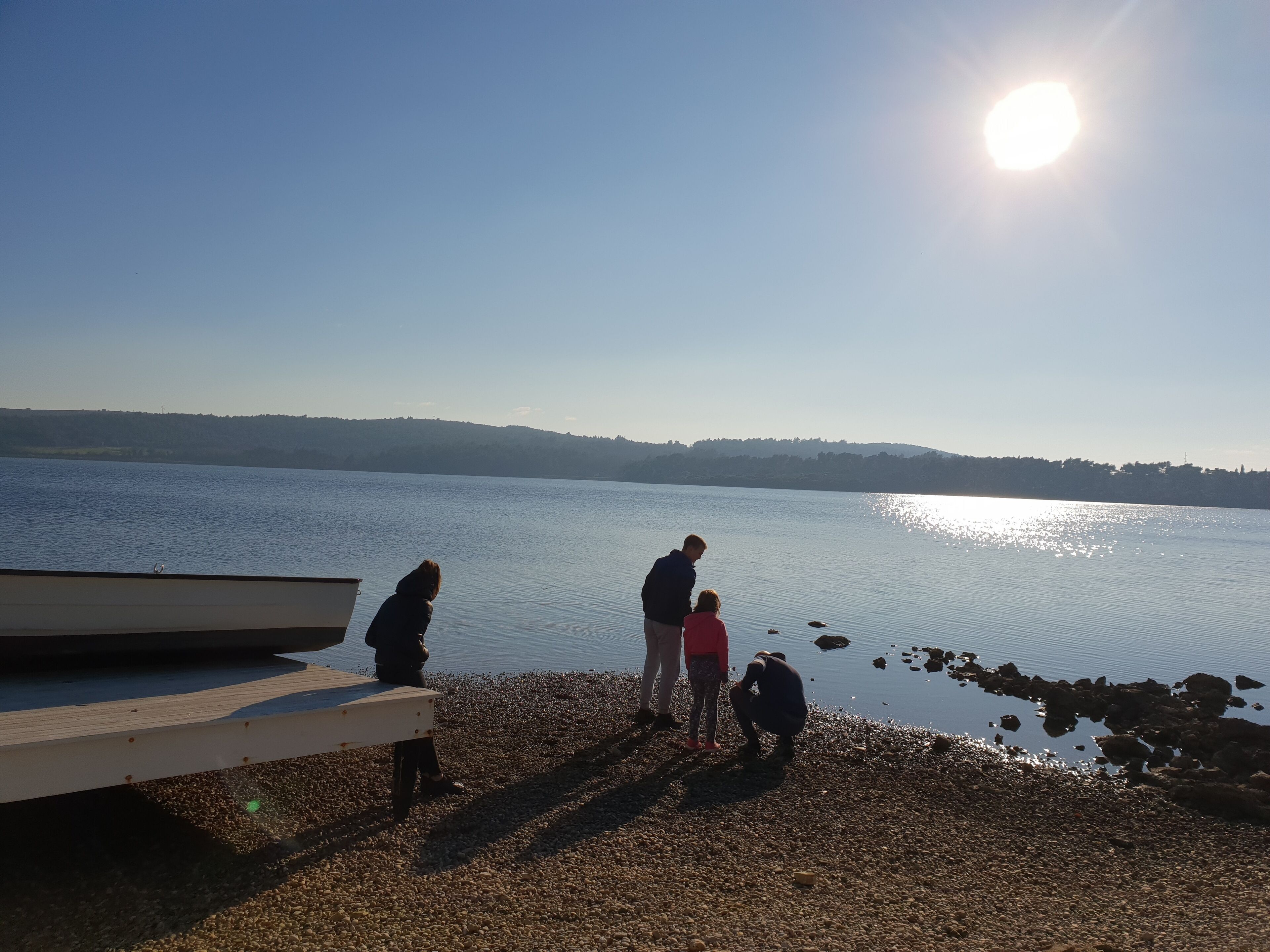 Ein Kiesstrand mit einem Holzsteg und einem ruhigen See.