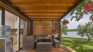 Un espace extérieur abrité, doté de mobilier en osier, d’un distributeur d’eau et offrant une vue sur un lac.