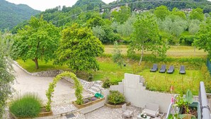 Un patio con suelo de piedra, mobiliario exterior y vistas a un jardín exuberante y casas en la ladera.
