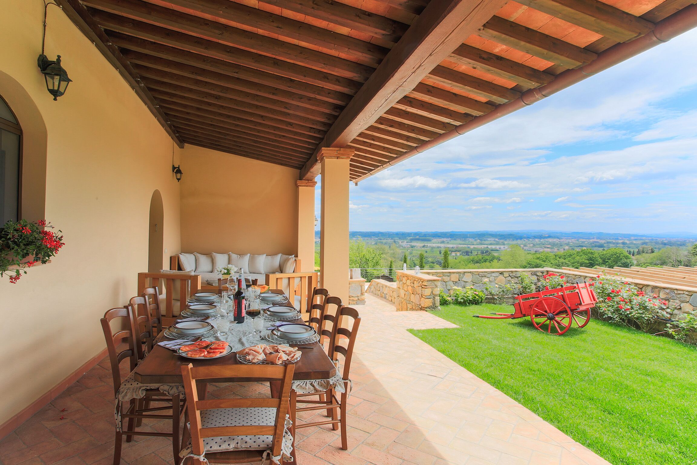 A covered patio with a dining table set for six, outdoor seating, and a view of the countryside.
