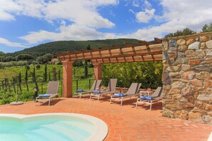 A poolside area with lounge chairs and a pergola, overlooking a vineyard and hills. - Casa di Dante (Vicopisano)