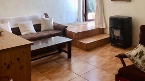 Un salon avec un canapé, une table en bois, une chaise, un radiateur et une fenêtre avec des rideaux.