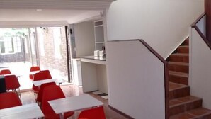 A modern interior with white tables and red chairs, a staircase, and a view of the outside. - Hotel Barrio Yungay (Santiago)